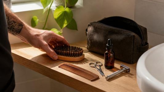 Kit barbe posé sur une étagère de salle de bain : brosse, peigne, ciseaux, huile, rasoir et trousse de toilette