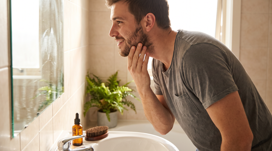 Homme qui observe sa barbe en train de pousser devant le miroir de sa salle de bain, comment faire pousser sa barbe plus vite