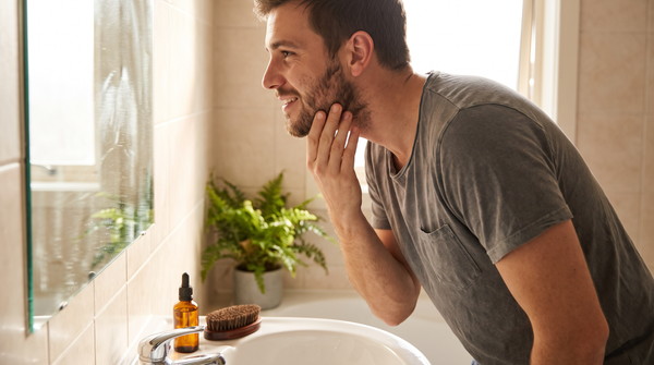 Homme qui observe sa barbe en train de pousser devant le miroir de sa salle de bain, comment faire pousser sa barbe plus vite