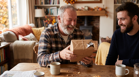 Idée cadeau pour papa : un père barbu rit en ouvrant un cadeau à table à côté de son fils